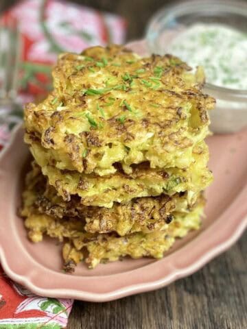 Golden cabbage fritter stacked on pink dish with cream dip.