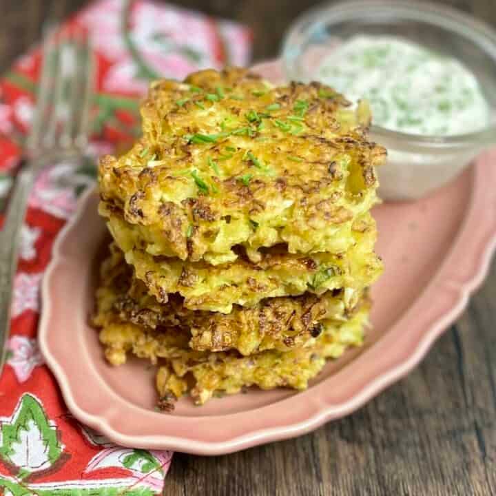 Golden cabbage fritter stacked on pink dish with cream dip.