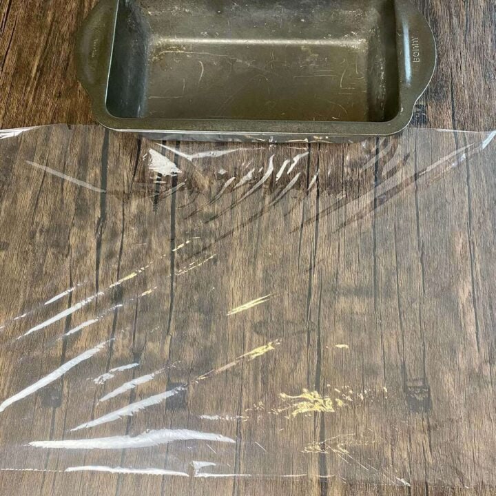 A loaf pan next to a piece of plastic wrap.