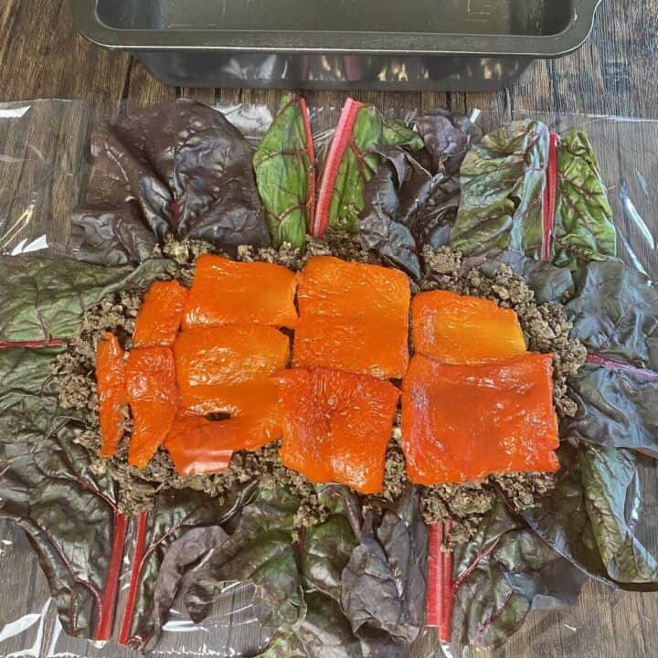 Swiss chard leaves laid on plastic wrap topped with duxelles and bell pepper.