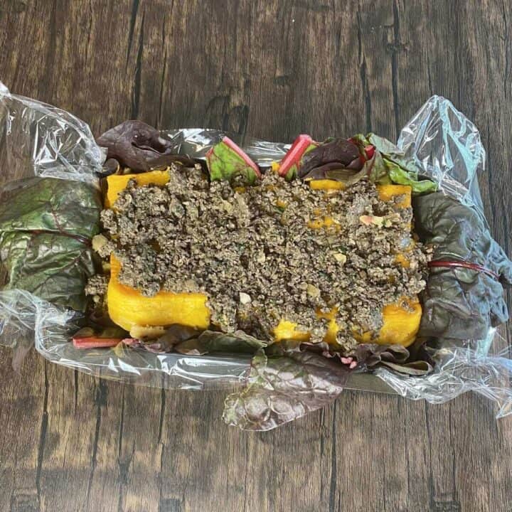 Plastic wrap-lined loaf pan filled with wellington stuffing ingredients.