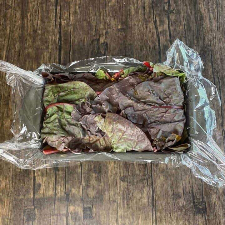 Plastic wrap-lined loaf pan filled with wellington stuffing ingredients.