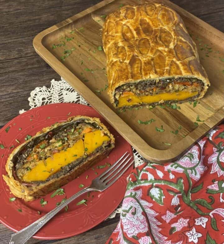 A vegetable wellington loaf on a wood platter with a slice on a plate.